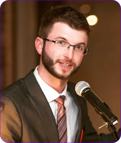 Man in a suit speaking into a microphone, representing Frayze Technologies Inc. at a local business event in Thunder Bay.